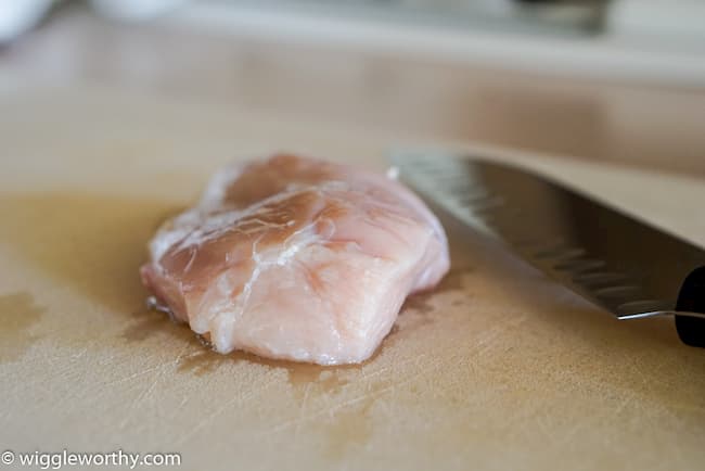 Raw chicken breast on cutting board beside sharp knife